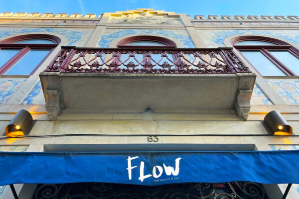 Entrance to 'Flow' restaurant with blue awning and white lettering, marble-like balcony above with red patterned railings.